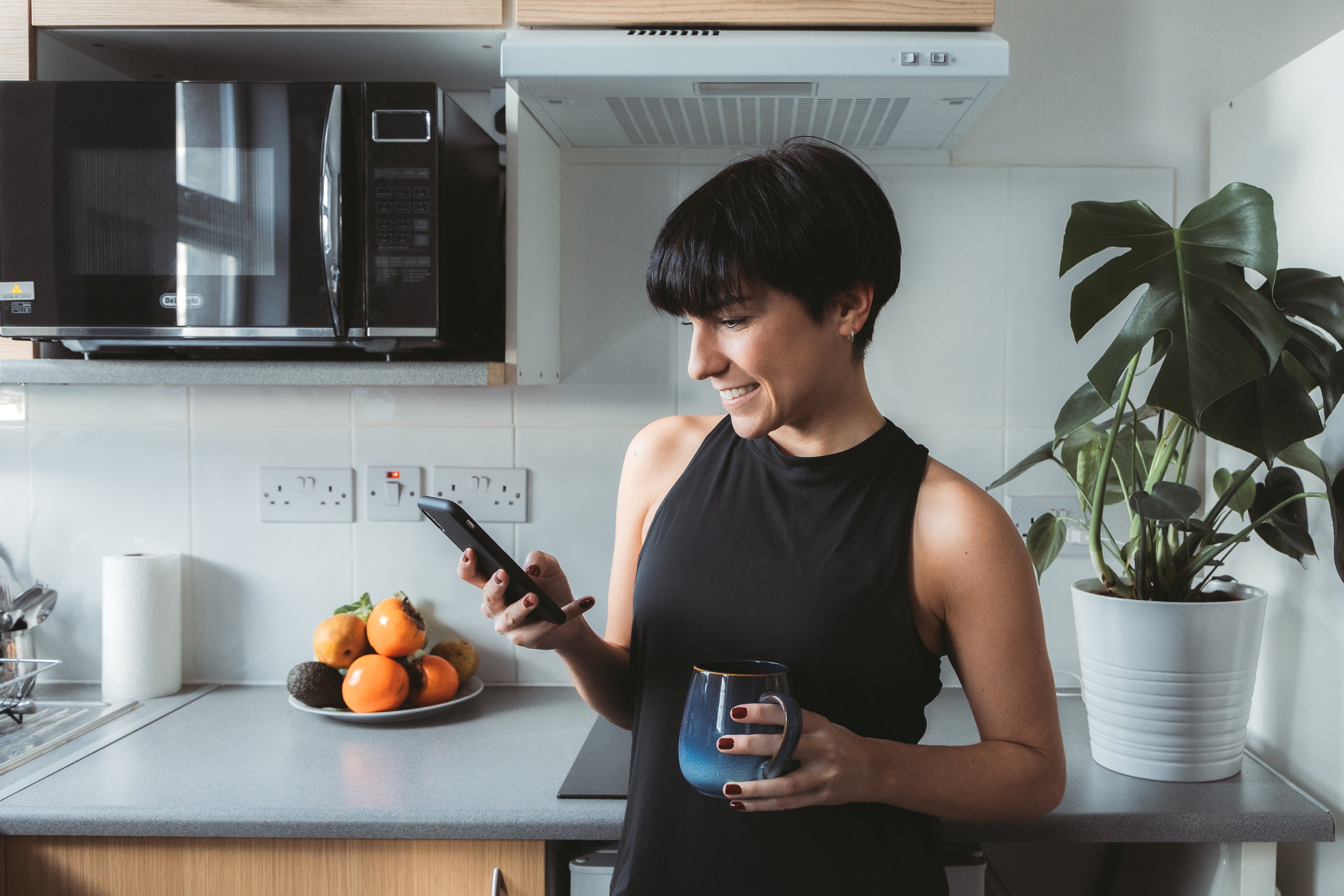 woman-stands-in-the-kitchen-and-smiles-while-using-cell-phone.jpg